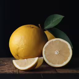two lemons and one is sliced in half with leaves on the top