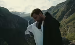 a man standing on a mountain overlooking a waterfall