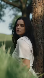 a beautiful young woman in white leaning against a tree