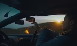 the sun sets in a rural setting, behind the wheel of a car