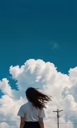 a girl walking down a dirt path under a cloudy sky