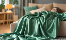 a woman is lying on the sofa under a green blanket