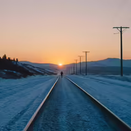 man walking down the railroad tracks at sunrise