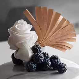 there are flowers and a black berry in front of a paper umbrella
