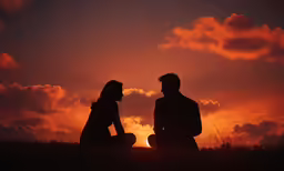 two people are sitting and talking on the hill