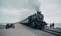 a black train blowing smoke on tracks near water