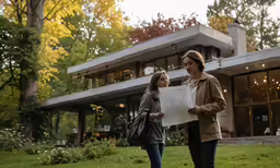 two women holding paper in front of their home