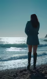 a woman is standing on the shore of a beach near some waves