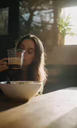 a girl sitting at a table drinking from a glass