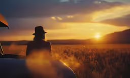 a woman in a hat looks out at a field of wheat
