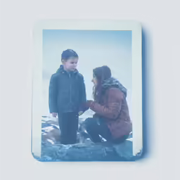 a young man kneeling down next to a woman in winter clothing