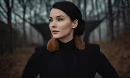 a woman standing in front of trees with a coat and earring