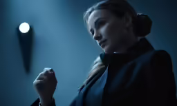 a woman wearing a black coat is standing in a darkened room