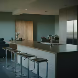 a long, white counter with chairs is in the middle of a gray kitchen
