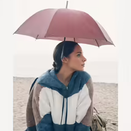a woman is sitting under an umbrella on the beach
