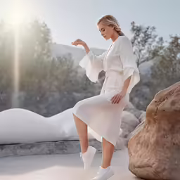 a woman poses in a white outfit by a rock