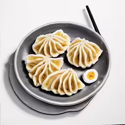 some dumplings with egg on the side and chopsticks sitting on the table