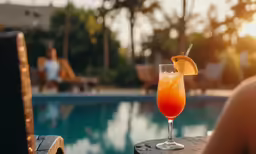 a drink sits near a swimming pool at sunset
