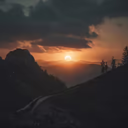 the sun set over some hills with dark clouds