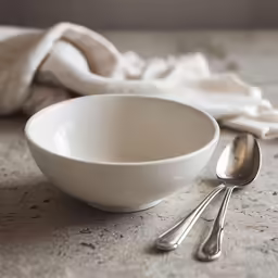 there is a white bowl and two silver spoons next to each other