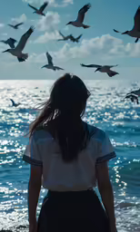 a woman is walking along the water and a lot of birds are flying overhead