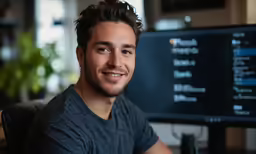 a smiling man sitting in front of a computer