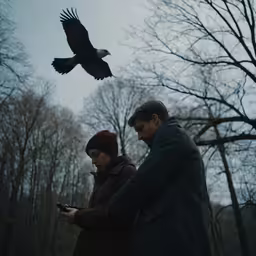 two people look at their cell phones near a bird that is flying