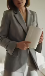 a woman in grey jacket standing next to a bed
