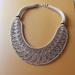 the necklace is attached to a wooden table,a necklace that is attached to a white surface,the silver necklace has beads and silver filigrees on it,a large silver necklace with a spiral design on it,a necklace is displayed on a table