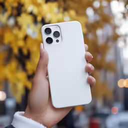 a hand holding a white case for a cellphone in front of some autumn foliage