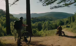 two people sit near a dirt path in a forest