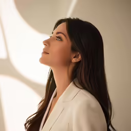 a woman looking off into the distance wearing a white blazer and pearl necklace