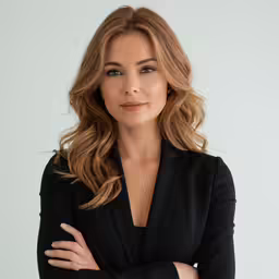 a woman in a black jacket and tie with her arms crossed