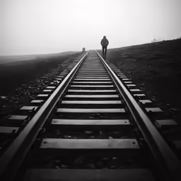 man standing on railroad track looking back at sky