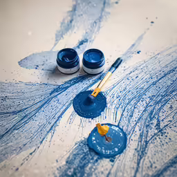 the brushes are laying beside two blue paint cups