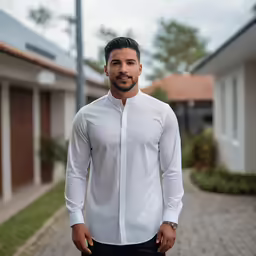 a man standing outside in white dress clothes and looking at the camera