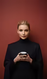 a woman standing against a red wall and holding a cell phone