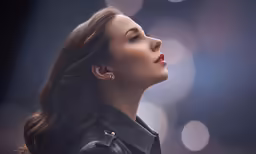 a woman with long hair is wearing a leather jacket and earrings