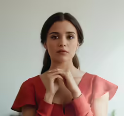 a woman in red top with her hands clasped against her chest