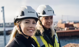 two women standing by the ocean wearing helmets