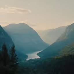 a small lake surrounded by mountains under a cloudy sky