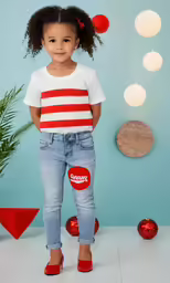 young girl in a striped t - shirt stands with red ornaments hanging from the back
