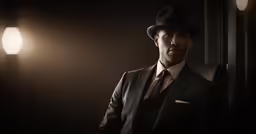a man in a suit and hat standing near a lamp
