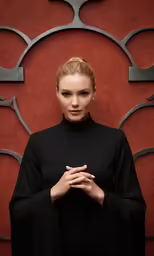 a woman wearing black in front of a red wall