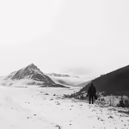 black and white photo of person walking on snow covered mountains