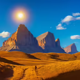 a lone hiker walks through an arid field with tall mountain towering into the distance