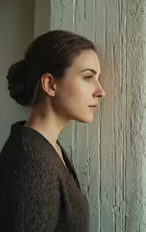 a woman standing next to a wall with a ponytail up and her eyes closed