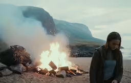a woman walking next to a burning bonfire