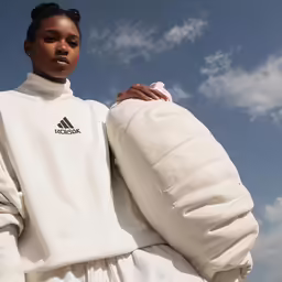 a woman in a white top holds a jacket up