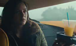 a woman looking out the window while holding a drink in her hand